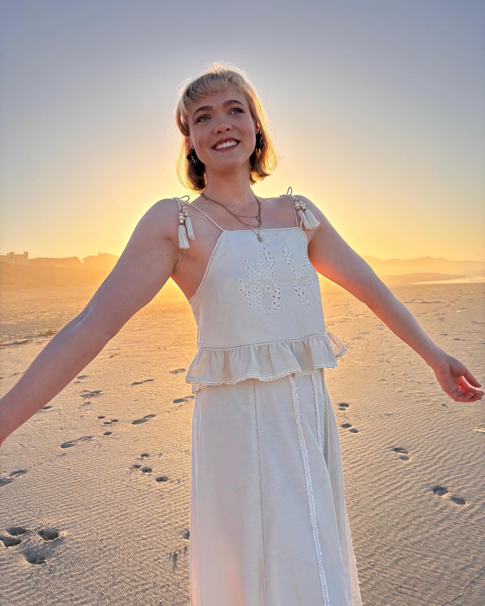 Elmarie van der Merwe, occupational therapist, smiling on a beach at sunset with her arms open